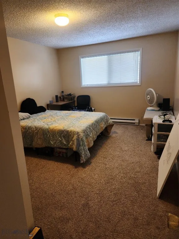 Carpeted bedroom with a textured ceiling and a baseboard heating unit