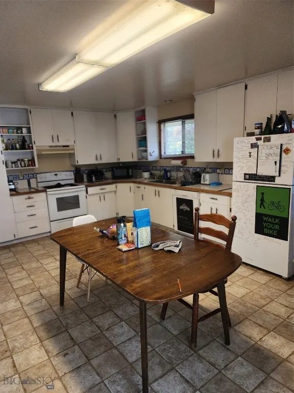Kitchen with wine cooler, fridge, range hood, white cabinets, and stove