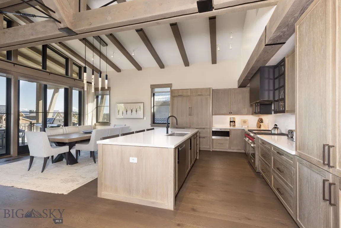 Kitchen with beam ceiling, sink, dark hardwood / wood-style floors, range with two ovens, and a kitchen island with sink