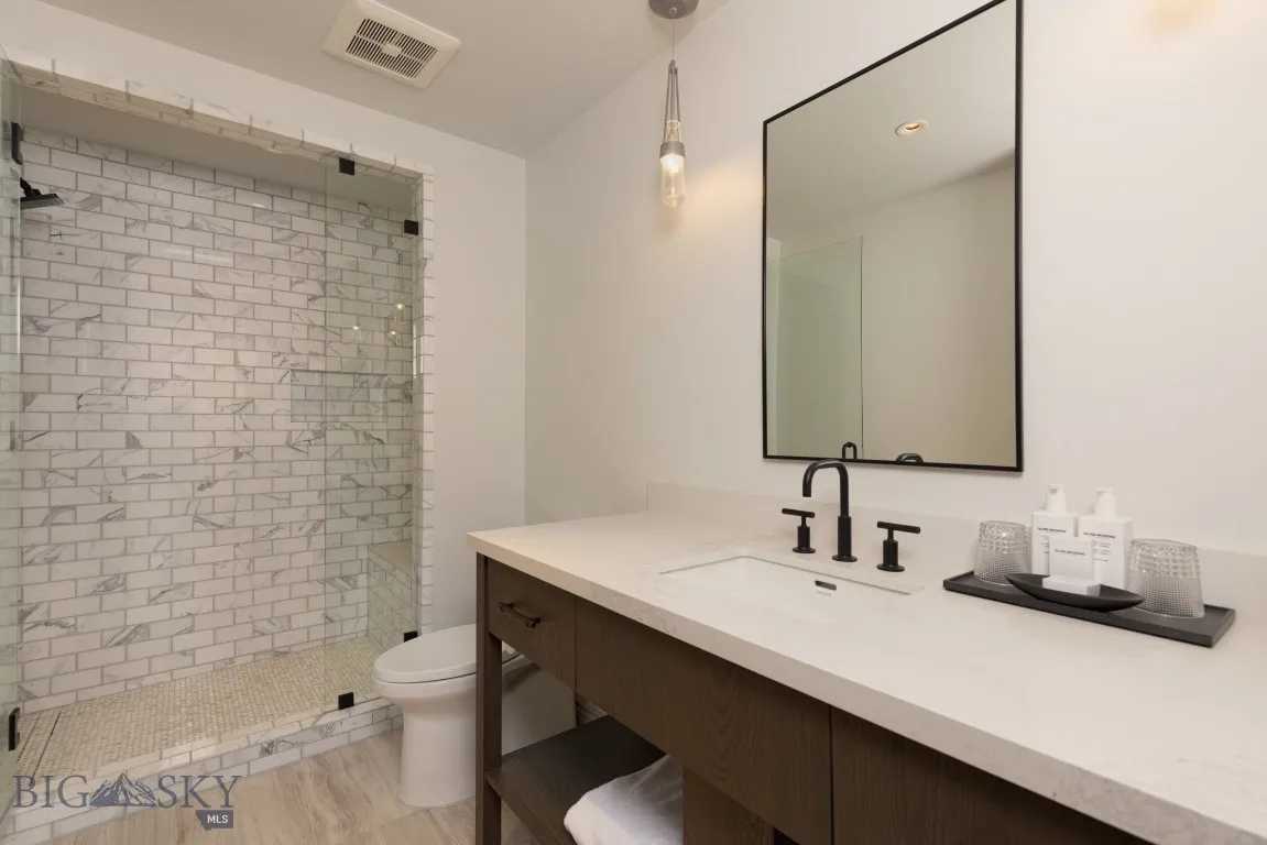 Bathroom with a tile shower, vanity, toilet, and hardwood / wood-style floors