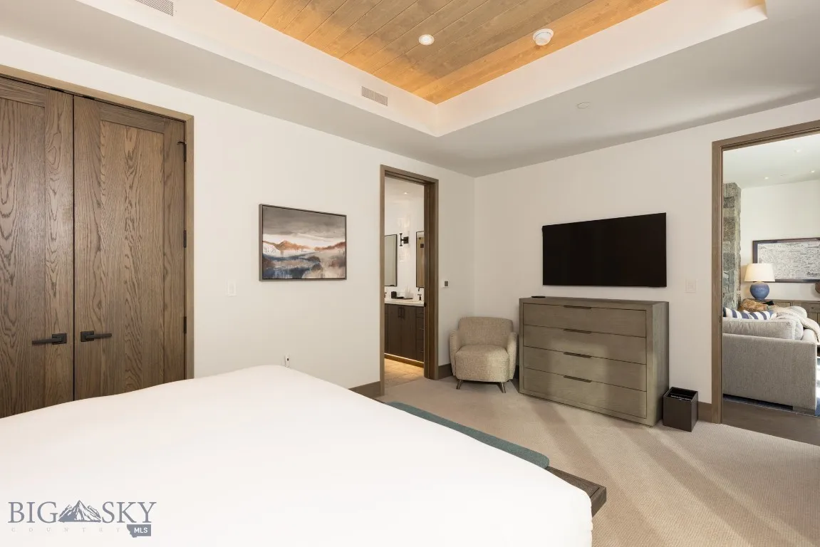 Bedroom featuring light carpet, ensuite bathroom, a tray ceiling, wood ceiling, and a closet