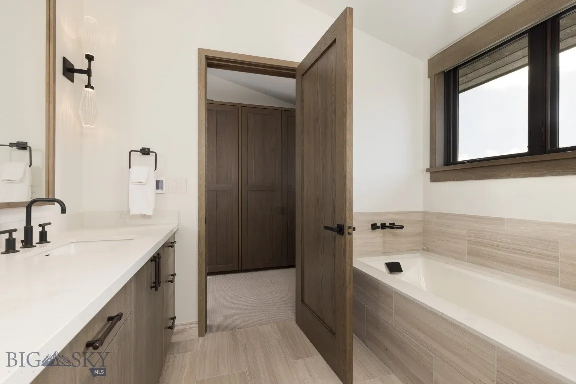 Bathroom featuring tile patterned floors, tiled tub, vanity, and lofted ceiling