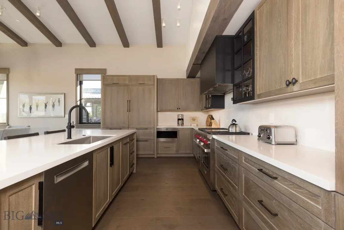 Kitchen with appliances with stainless steel finishes, dark hardwood / wood-style floors, beam ceiling, and sink