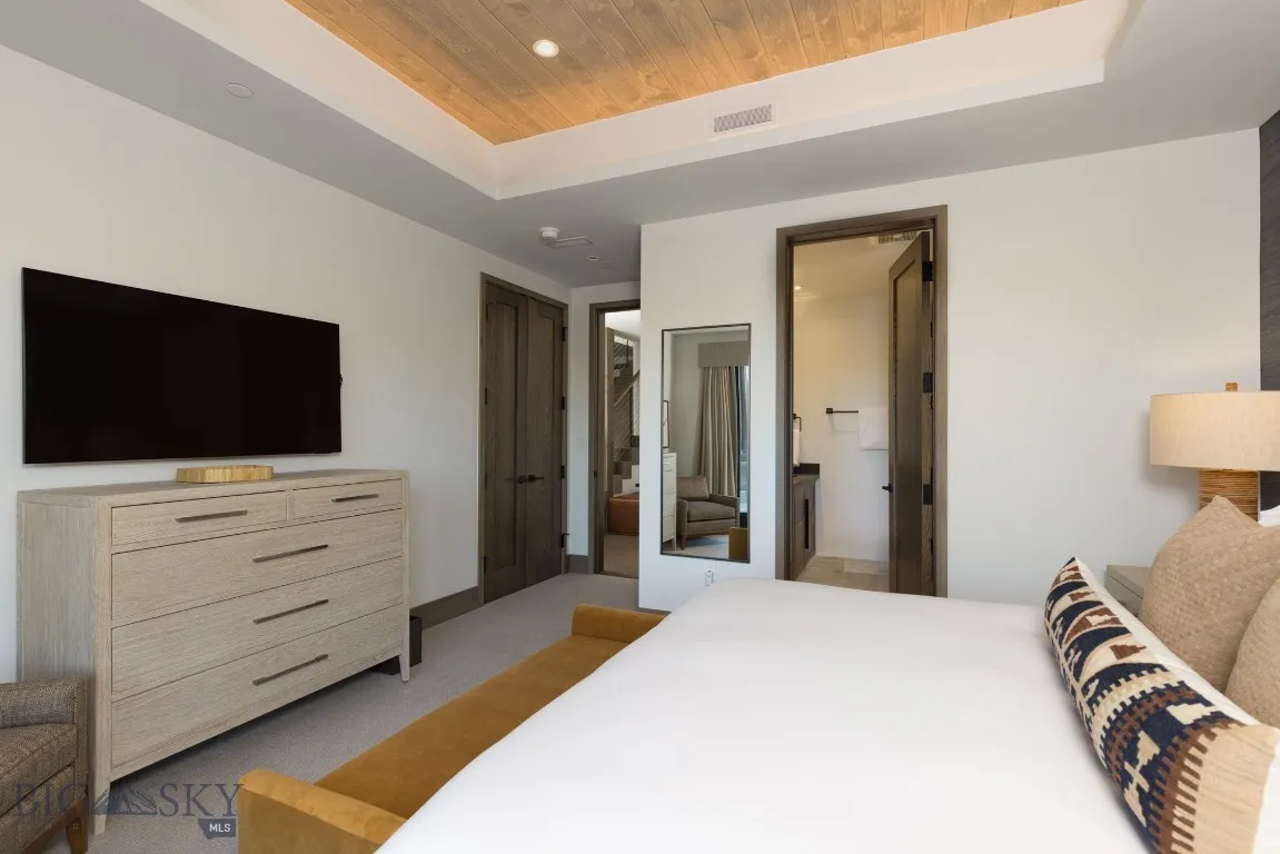 Bedroom featuring a tray ceiling, connected bathroom, wood ceiling, and light colored carpet