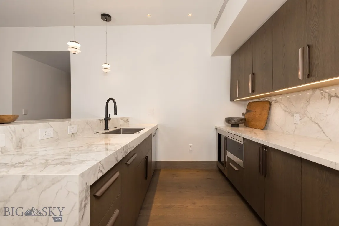 Kitchen featuring backsplash, sink, light stone counters, decorative light fixtures, and dark hardwood / wood-style flooring