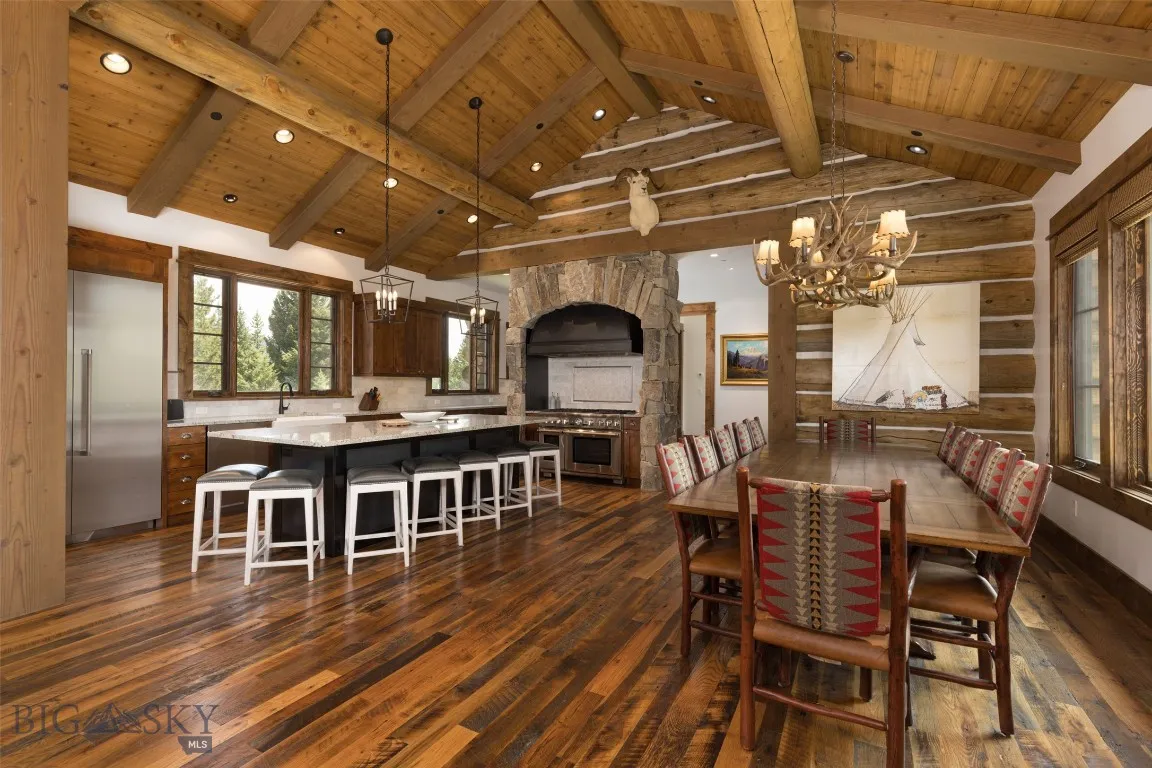 Spacious open-concept dining and living area featuring vaulted wood ceilings, a grand stone fireplace, and seating for large gatherings—perfect for entertaining in rustic luxury.