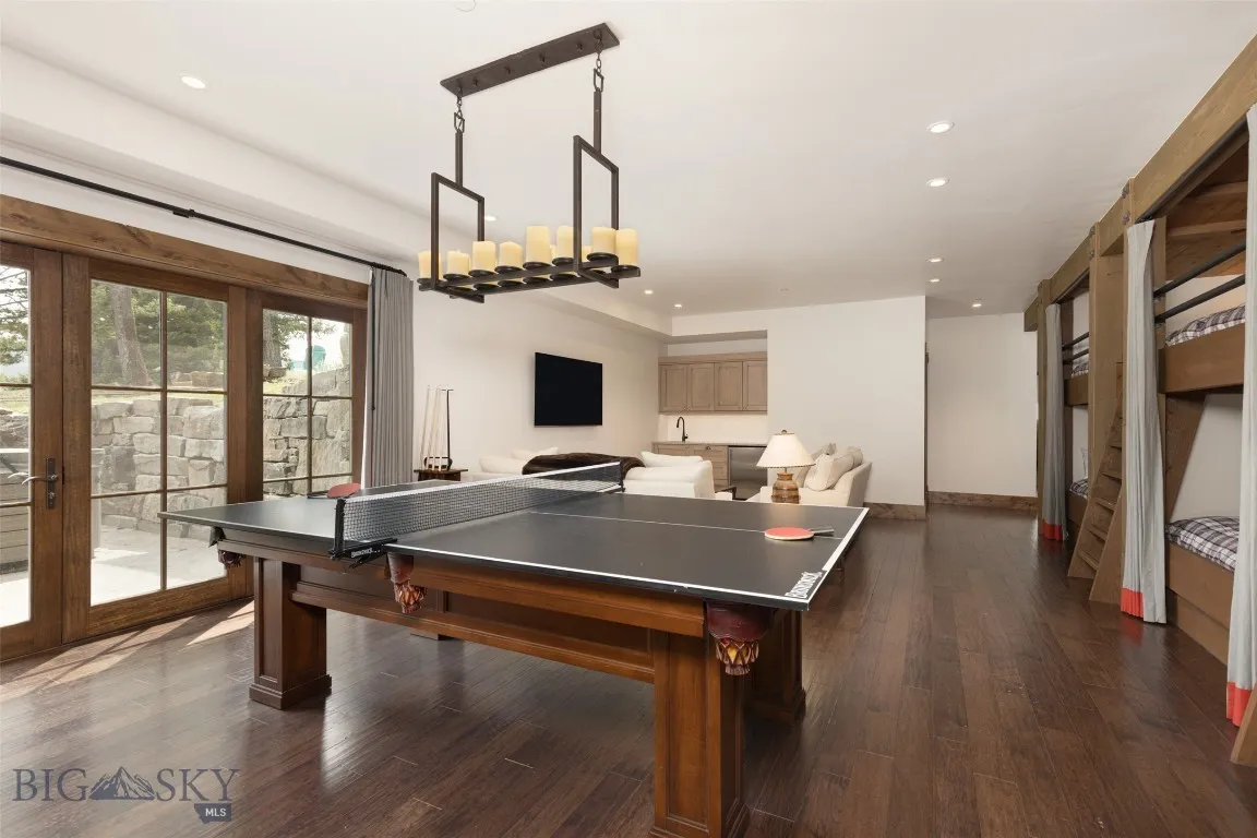 Versatile lower-level bunkroom and playroom featuring built-in sleeping quarters, a spacious lounge area, game table, wet bar, and direct patio access—perfect for entertaining guests or hosting family fun.