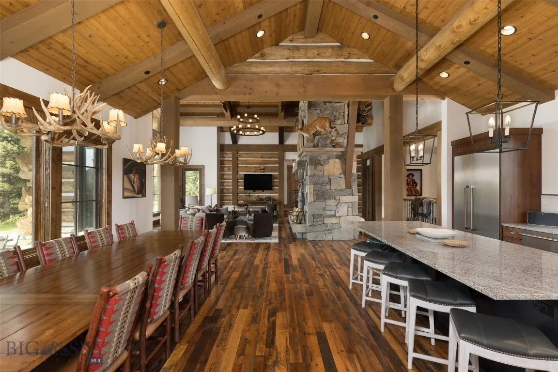 Spacious open-concept dining and living area featuring vaulted wood ceilings, a grand stone fireplace, and seating for large gatherings—perfect for entertaining in rustic luxury.
