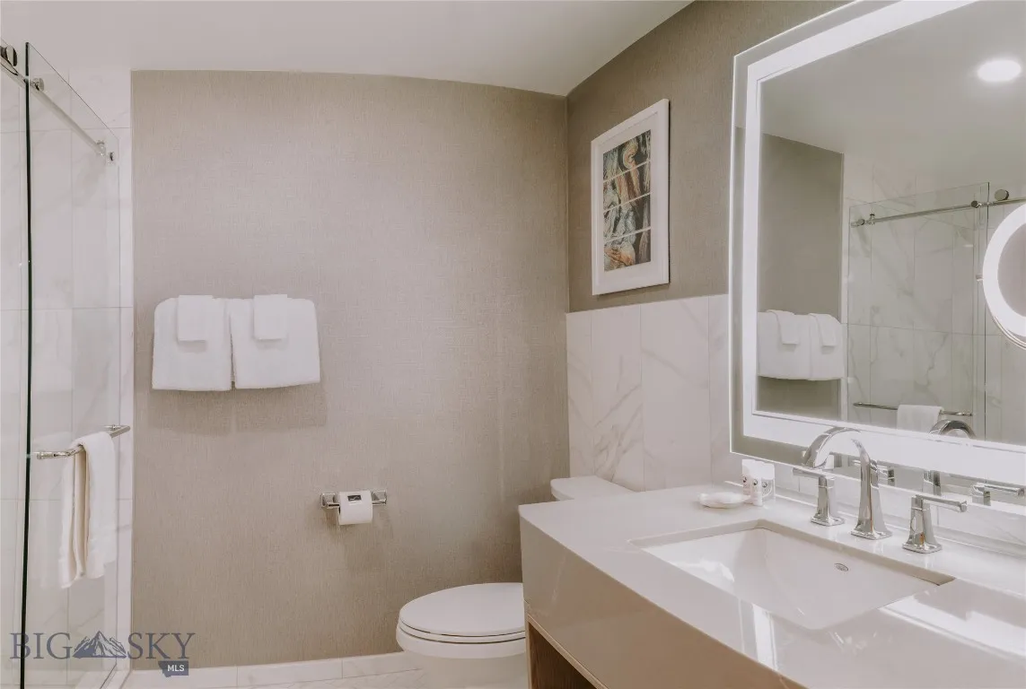 Spa-inspired bathroom featuring a glass-enclosed shower, illuminated vanity mirror, and marble-style tile finishes.