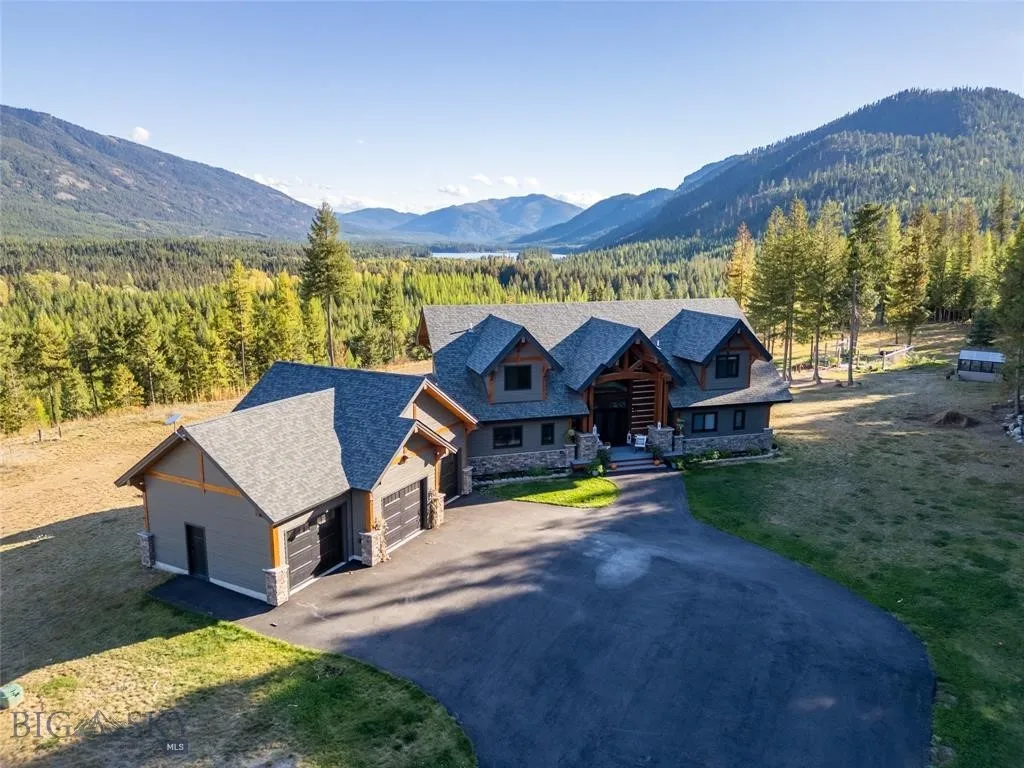 View of front of home with a front lawn, stone siding, a mountain view, a view of trees, and roof with shingles