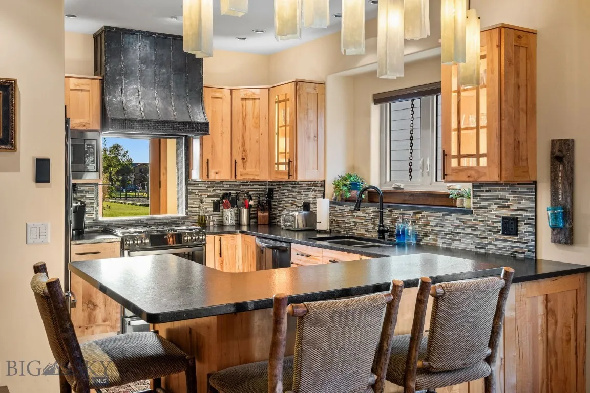 Kitchen with leathered granite countertops, black stainless appliances, custom pendant lighting, cabinet lighting, pot filler and a view of the park