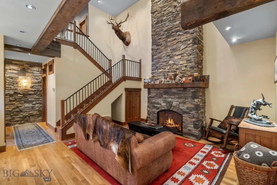 Living room featuring reclaimed lumber, stone fireplace, hardwood floors, custom lighting layout and a towering ceiling