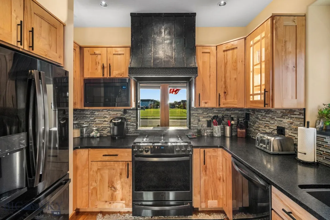 Kitchen with leathered granite countertops, black stainless appliances, pot filler and a view of the park