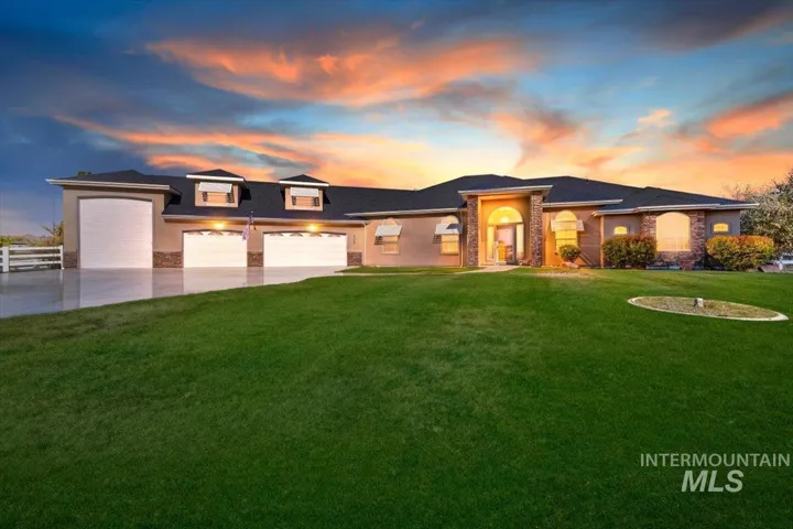 Single-story residence featuring a three-car garage, stone masonry accents, arched window detailing, and a covered entry, set against a expansive manicured lawn