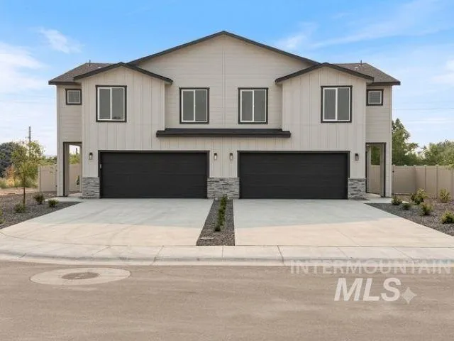 Contemporary duplex exterior featuring light-colored siding, black-framed windows, dark garage doors, and stone accents