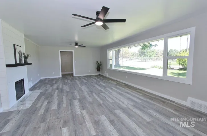 Spacious living area featuring wood-finish flooring, a white shiplap fireplace with a dark mantel, and two ceiling fans
