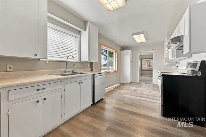 Kitchen featuring white cabinetry, light-toned countertops, a stainless-steel sink with a high-arc faucet, and wood-finish flooring