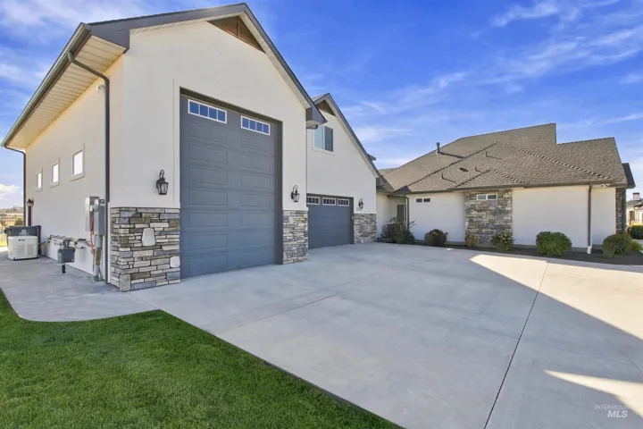 Exterior featuring light-colored stucco, stone accents, dark gray garage doors with windows, and a multi-pitch roof