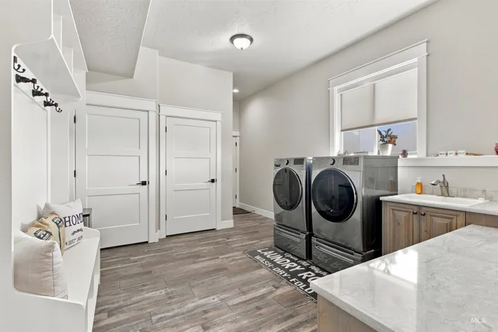 Built-in white storage bench with coat hooks, two panel doors with black hardware, wood-finish flooring, built-in cabinetry with a countertop, and a window