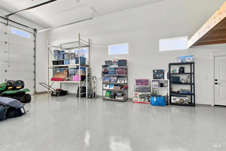 Epoxy-finished concrete flooring, overhead garage door with integrated windows, recessed ceiling lighting, and exposed wood beam framing