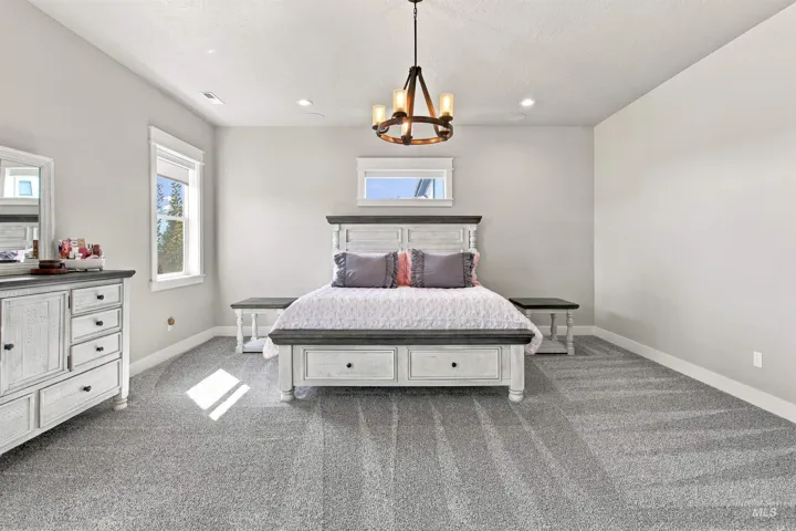 Spacious room featuring light gray walls, plush gray carpeting, recessed lighting, and a prominent chandelier