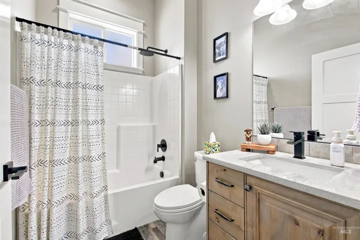 Wood-finish flooring, light-toned wall paint, vanity with wood-finish cabinetry, integrated sink with matte black faucet, and a tub-shower combination with matte black fixtures