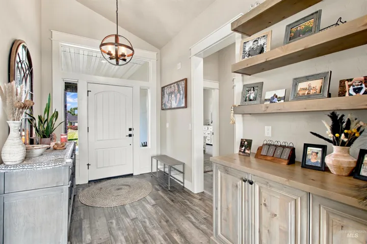 Entryway featuring a vaulted ceiling with a spherical chandelier, paneled front door with sidelights and transom, wood-finish flooring, and built-in wood shelving with lower cabinetry