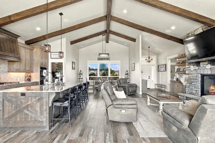 Vaulted ceilings with exposed wood beams, wood-finish flooring, a kitchen island with seating, stone fireplace, and built-in shelving