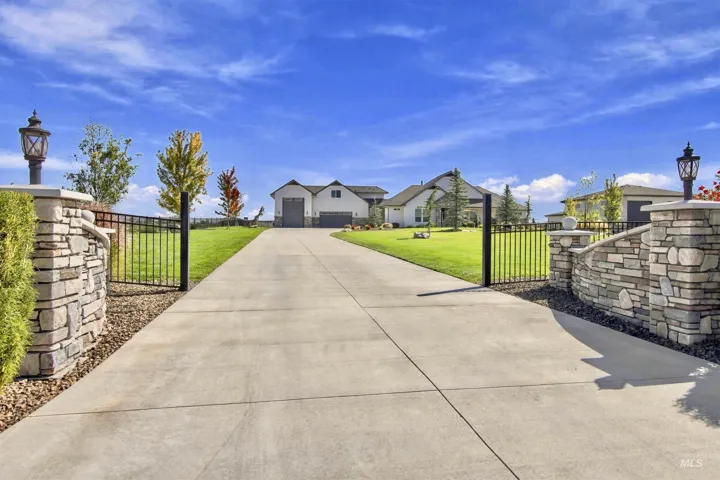 Concrete driveway with stone pillar entry featuring integrated lighting and wrought iron fencing