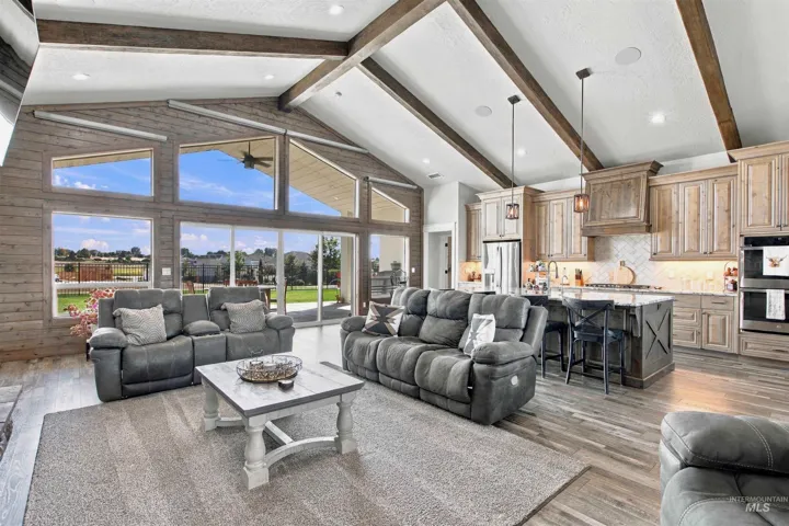 Vaulted ceiling with exposed wood beams, expansive floor-to-ceiling windows, wood-finish flooring, full kitchen with island seating, and built-in double ovens