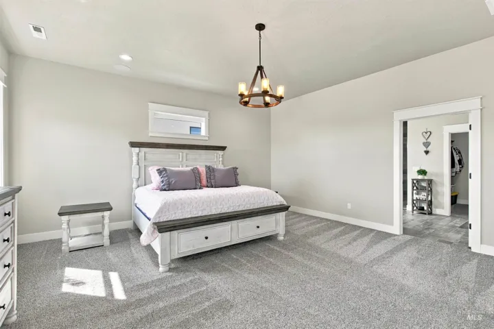 Expansive room featuring light gray walls, plush gray carpeting, and a rustic chandelier