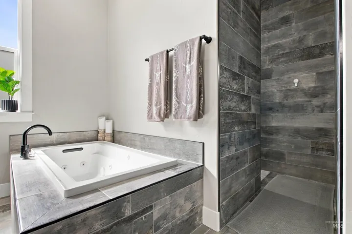 Built-in soaking tub with a matte black faucet, surrounded by large format tile
