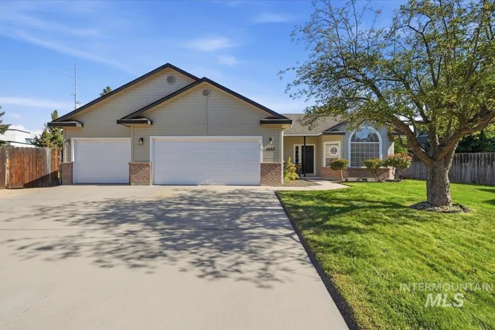Expansive concrete driveway, attached two-car garage, brick accents, arched window, and mature front yard tree