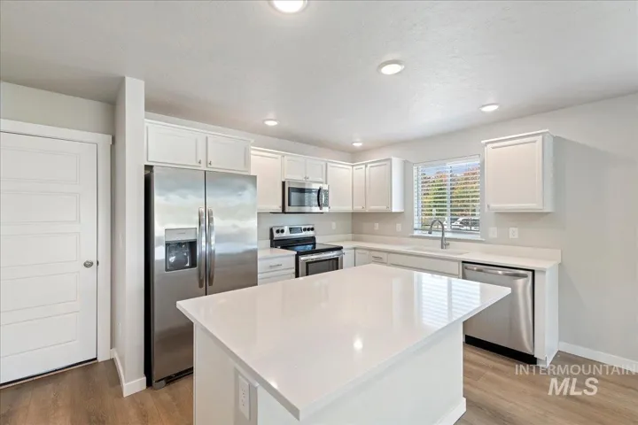 Kitchen featuring white cabinetry, solid-surface countertops, center island, stainless steel appliances, and wood-finish flooring
