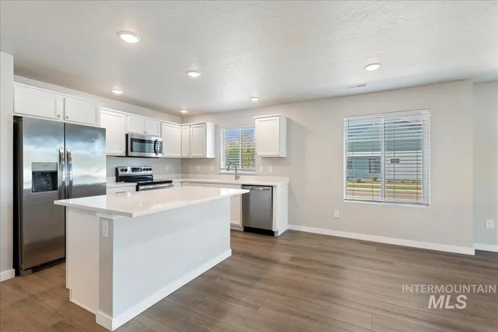 Kitchen featuring white cabinetry, an island with a light-toned solid surface countertop, stainless steel appliances, and wood-finish flooring