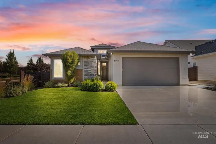 Contemporary exterior featuring a stone accent facade, attached garage, concrete driveway, and manicured front lawn with varied plantings