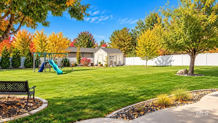 Expansive fenced backyard featuring a manicured lawn, concrete patio, detached storage structure, and mature deciduous trees