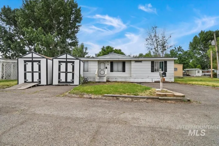 Single-wide manufactured home featuring white vinyl siding, a covered front entrance, and dual storage sheds with black and white trim
