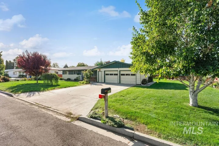 Front exterior featuring a two-car garage, concrete driveway, and expansive lawn with mature trees