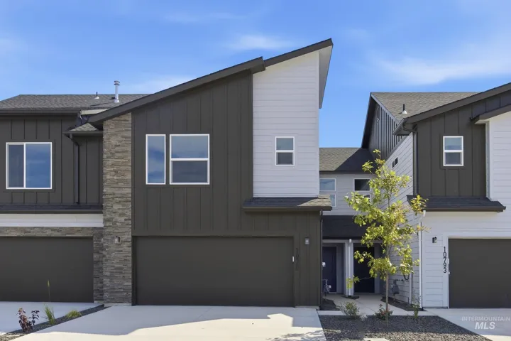 Modern architectural facade featuring vertical dark siding, light-colored accents, stone veneer detailing, and a prominent garage door