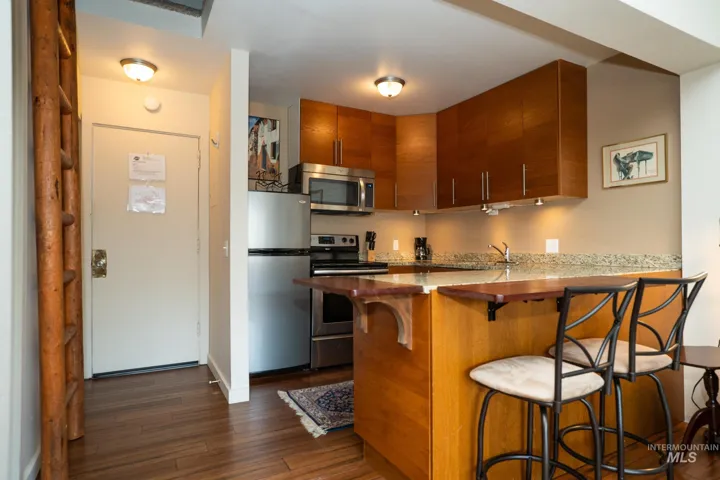 Kitchen with a kitchen bar, wood finish cabinets, a peninsula, stainless steel appliances, and dark wood-style floors