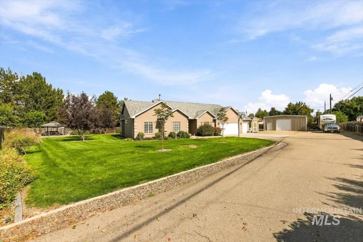Exterior featuring stucco siding, attached two-car garage, expansive manicured lawn, and a separate large metal outbuilding