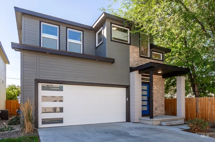 Modern exterior featuring gray horizontal siding, brick accents, a flat roof, an attached garage with translucent panels, and a covered entry with a blue door