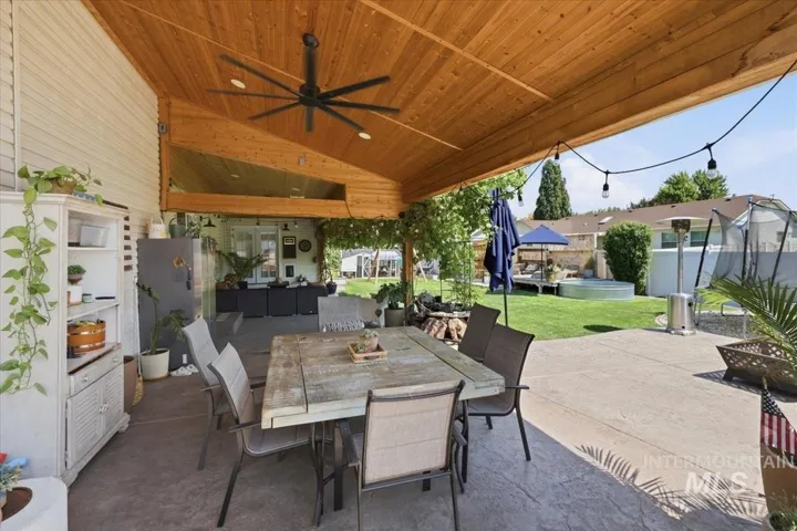 Expansive covered patio featuring a wood-finish ceiling, ceiling fan, and pendant lighting, anchoring a dining area with seating for multiple guests