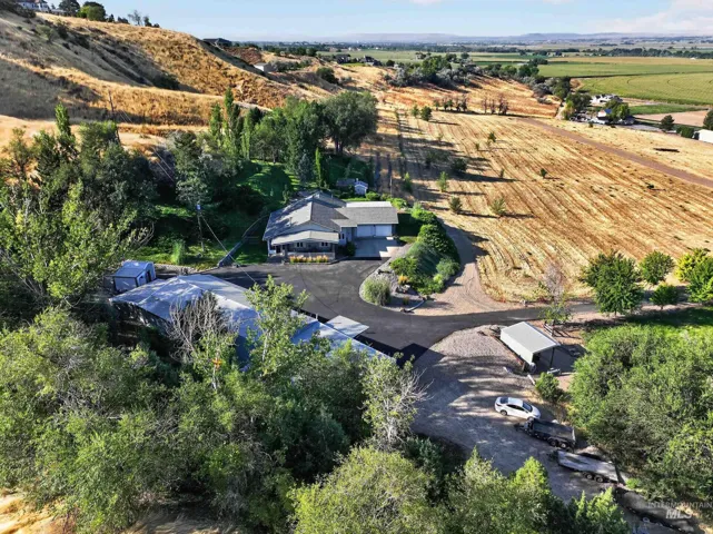 Expansive property featuring a residence with an attached garage, a separate outbuilding, and a gravel driveway