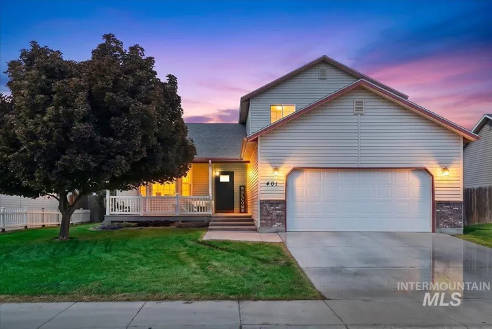 Siding exterior with stone accents, covered front porch, attached garage, concrete driveway, and a fenced yard
