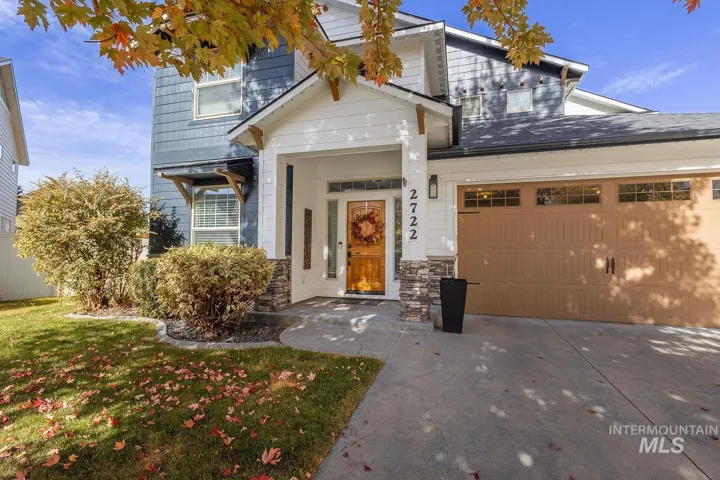 Two-story exterior featuring blue shingle siding, a white front entryway with stone column accents, and an attached multi-car garage with overhead windows