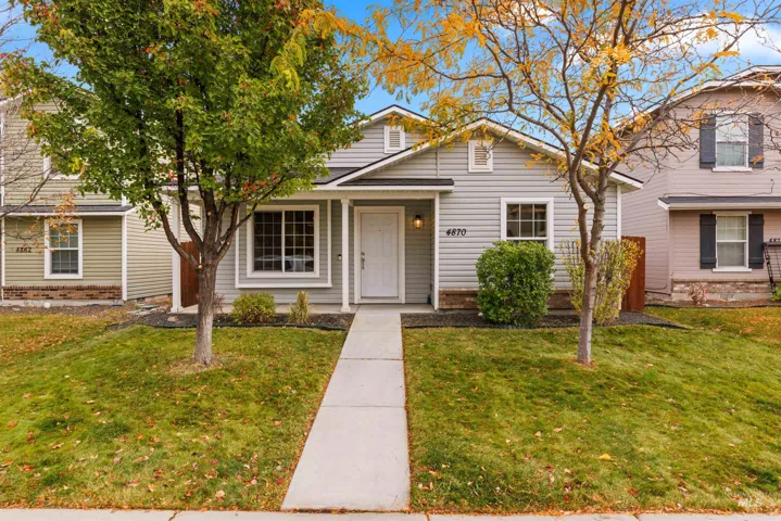 Light grey vinyl siding exterior featuring a covered front porch, concrete walkway, and landscaped front yard with mature trees