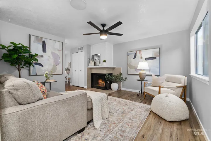 Living area featuring wood finished floors, ceiling fan, and a warm lit fireplace