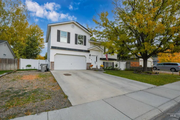 Two-story exterior featuring white horizontal siding, contrasting shutters, attached two-car garage, concrete driveway, and white vinyl perimeter fencing